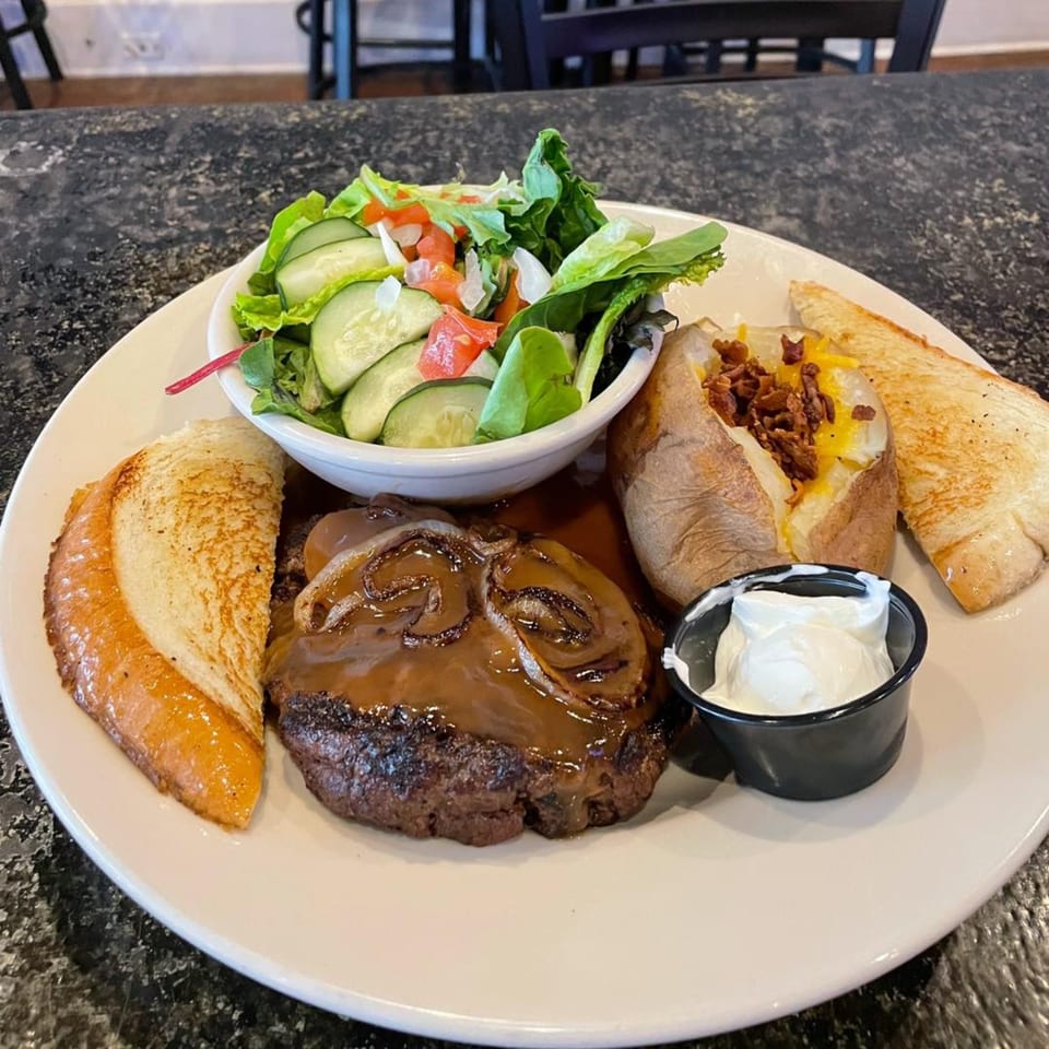 A steak with gravy and onions, a baked potato, side salad, and Texas toast on a white plate.
