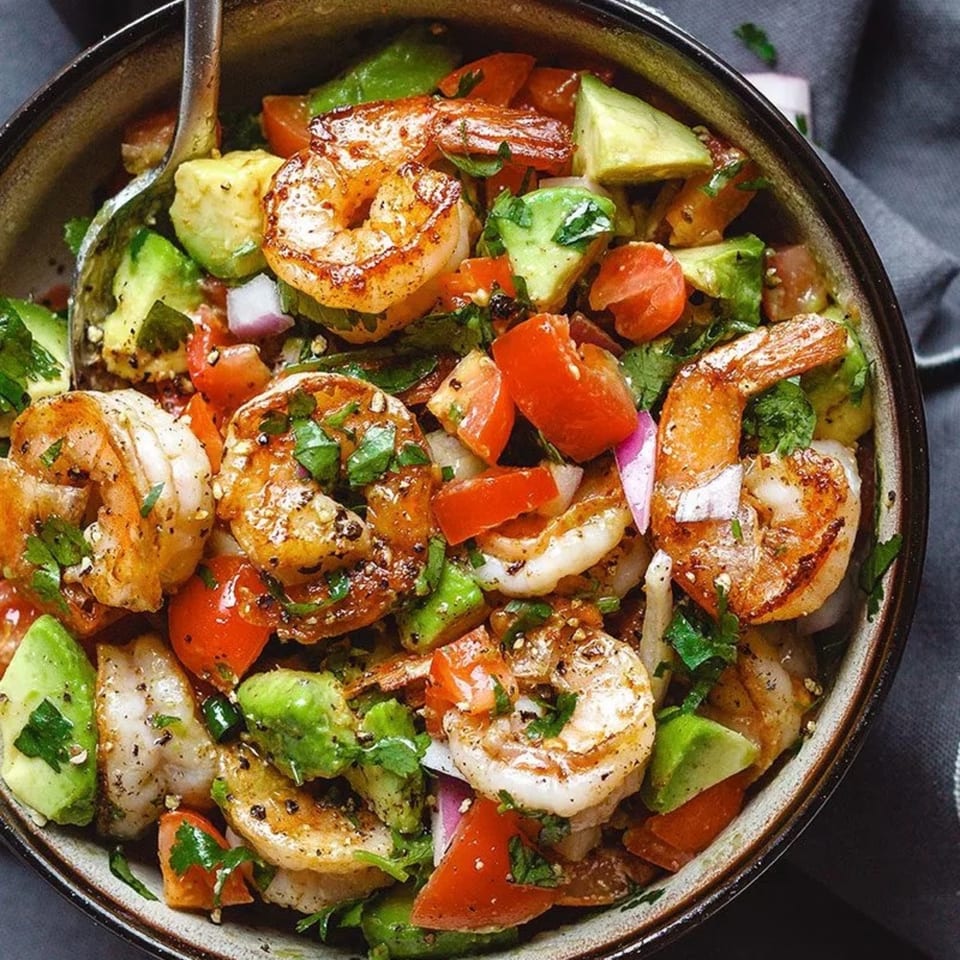 Close-up of a bowl of shrimp ceviche with avocado, tomatoes, and red onion.