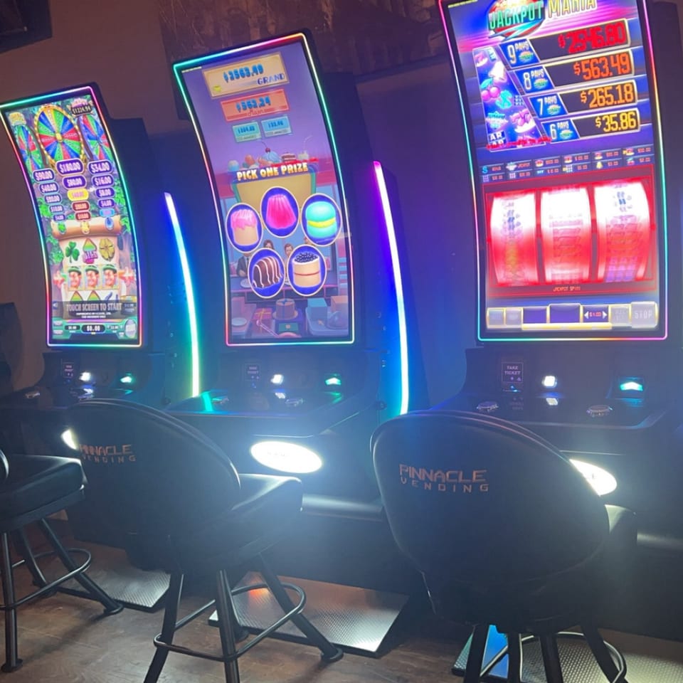 Three brightly lit slot machines with gaming chairs in a dark room at Brady Brewing Co.