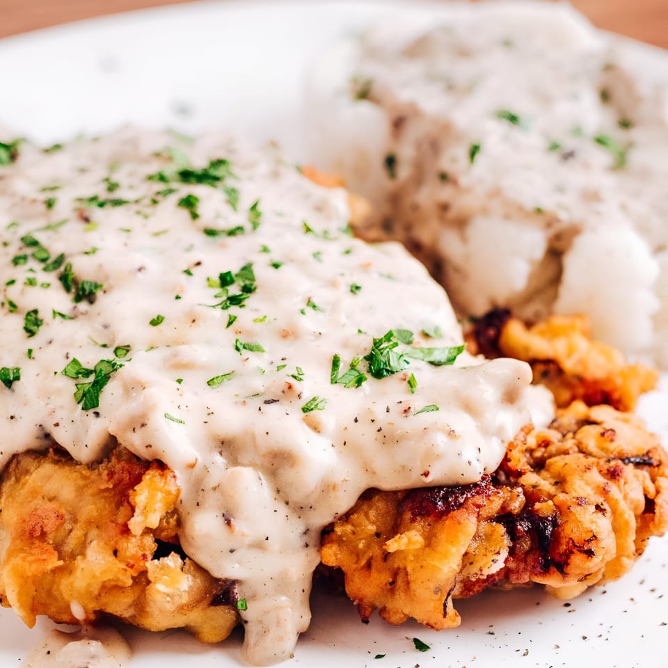 Crispy fried chicken steak smothered in creamy gravy and fresh parsley, with mashed potatoes.