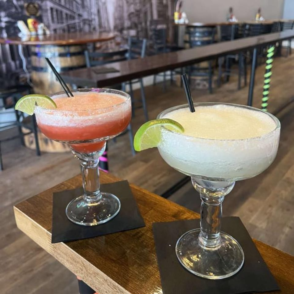 Two frozen margaritas, one red and one white, garnished with lime, on a wooden bar.