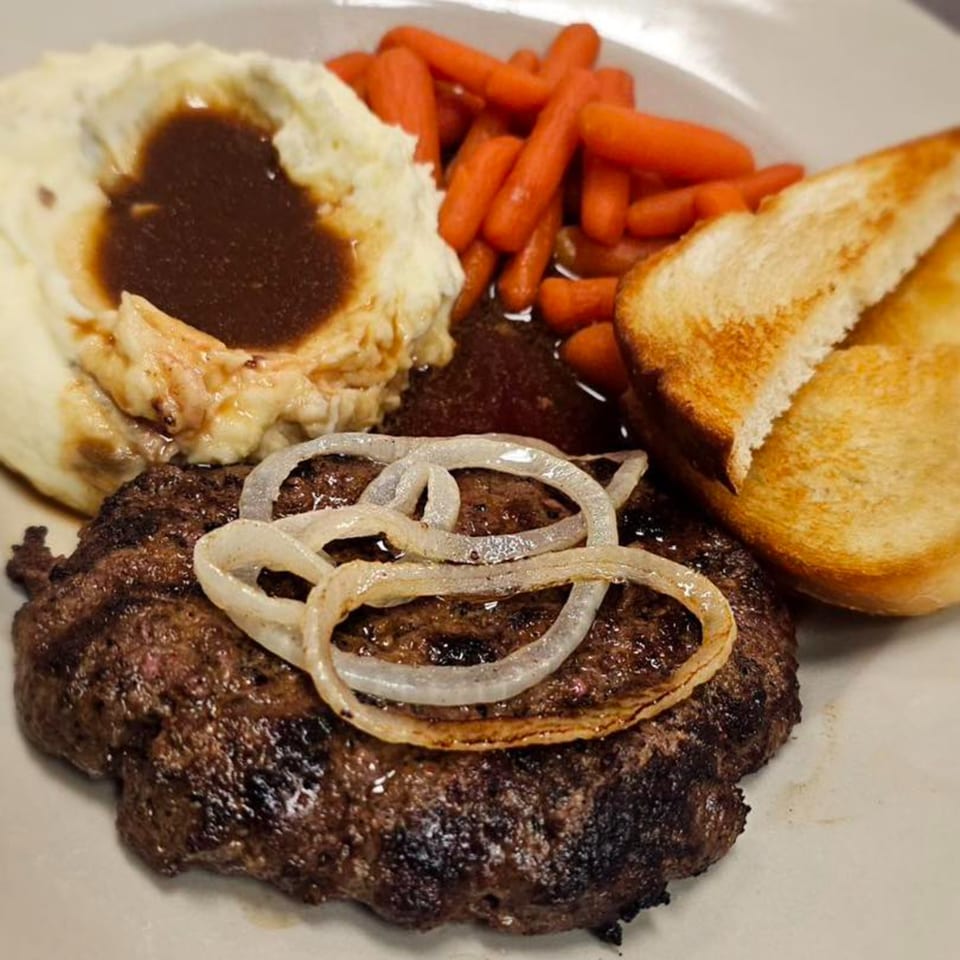 A Salisbury steak with grilled onions, mashed potatoes with gravy, baby carrots, and Texas toast.